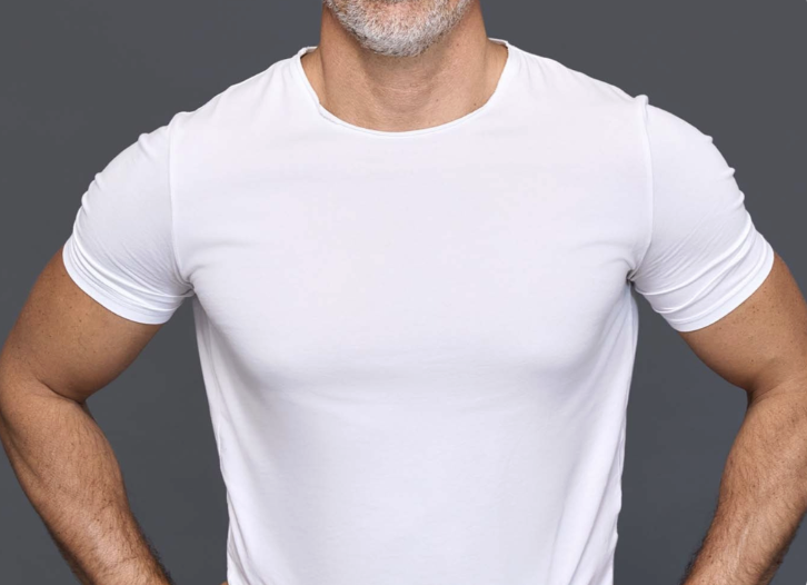 Homem com tórax liso, definido e sem volume mamário, de braços cruzados transmitindo confiança e segurança após a cirurgia de Ginecomastia na Clínica Orvia em São Paulo.